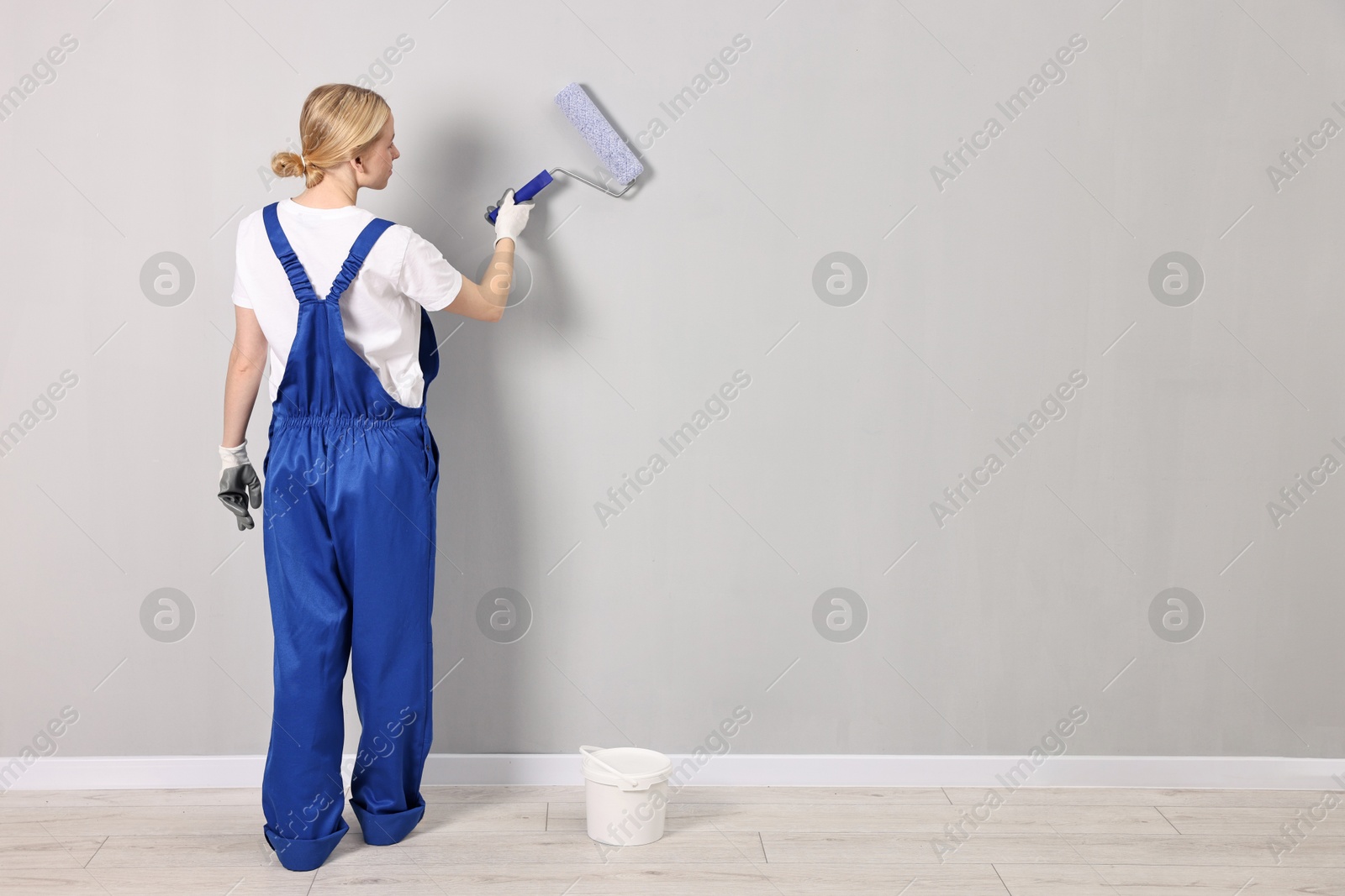 Photo of Female worker painting wall with roller indoors, back view. Space for text