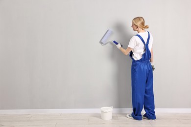 Photo of Female worker painting wall with roller indoors, back view. Space for text