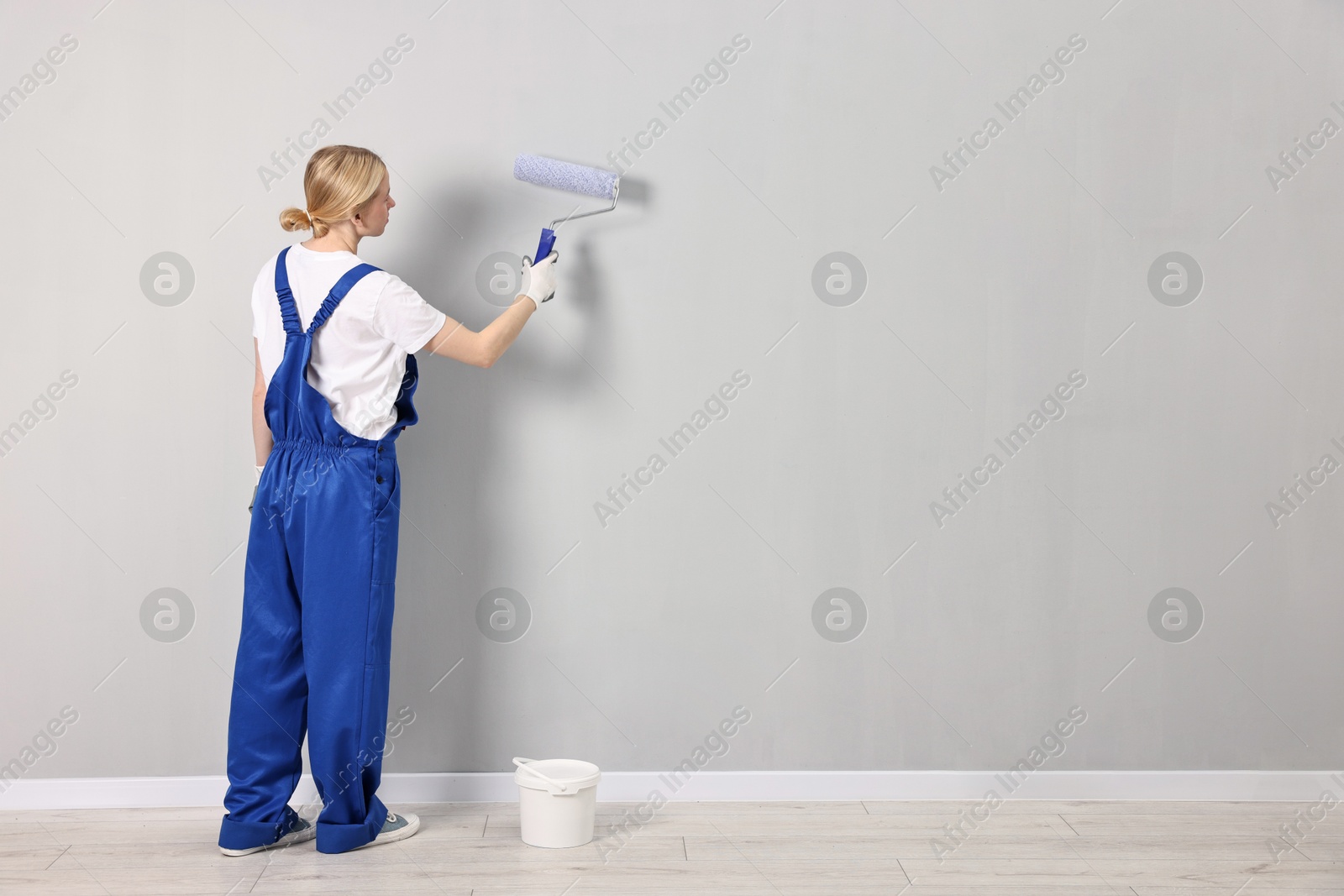 Photo of Female worker painting wall with roller indoors, back view. Space for text