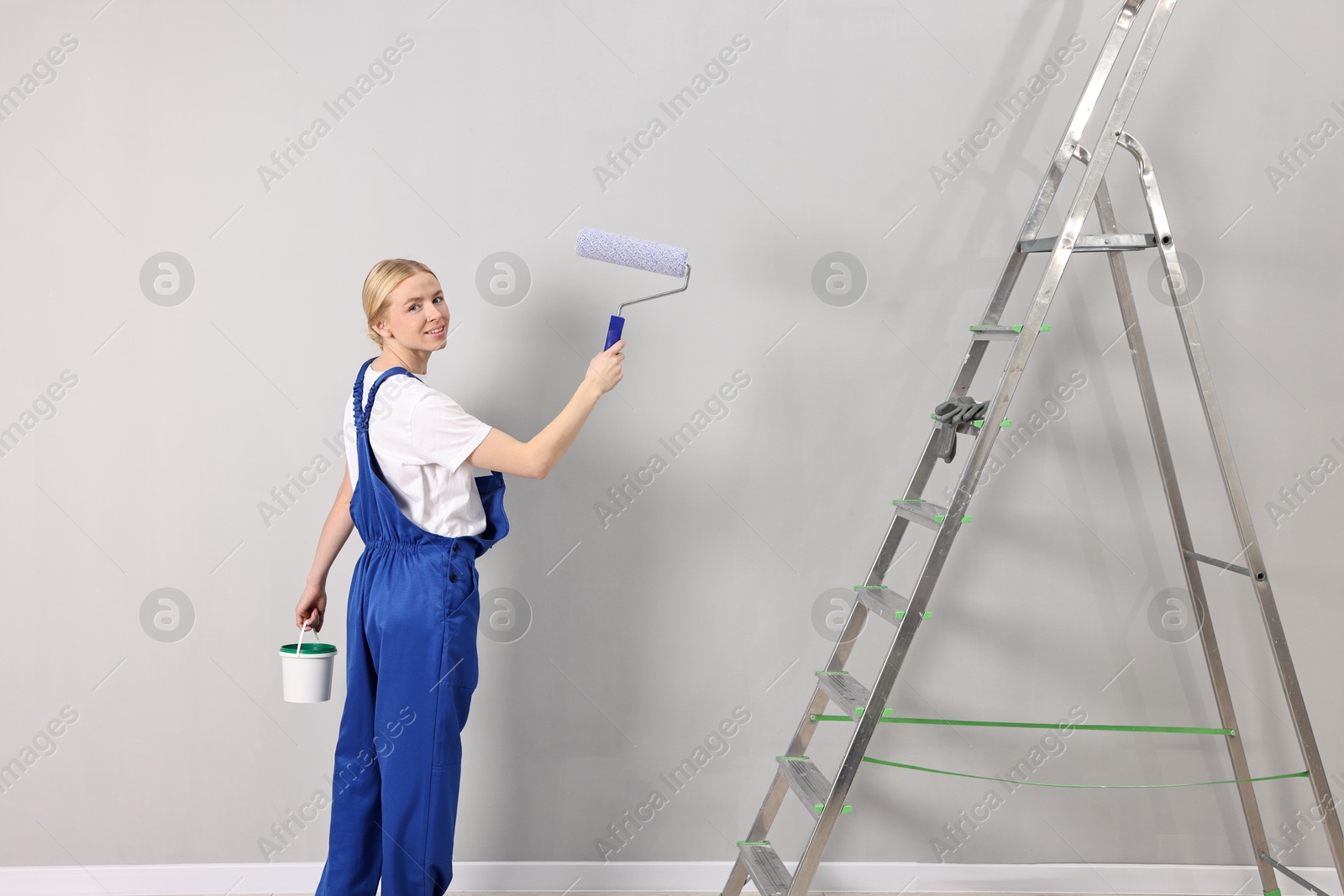 Photo of Smiling worker painting wall with roller near ladder indoors