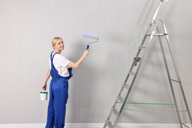 Photo of Smiling worker painting wall with roller near ladder indoors