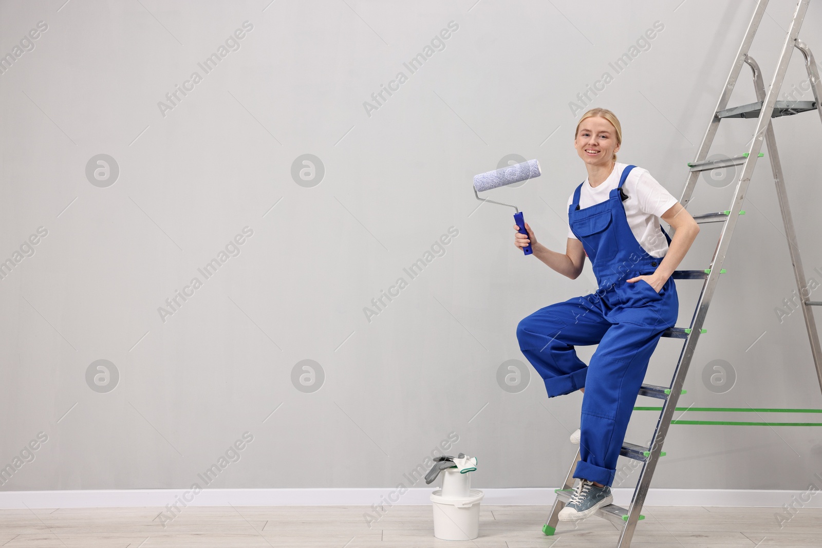 Photo of Smiling worker with roller posing on ladder indoors. Space for text