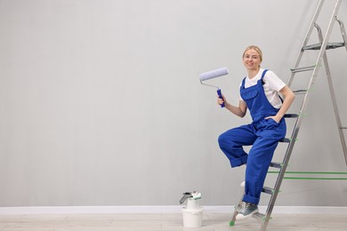 Photo of Smiling worker with roller posing on ladder indoors. Space for text