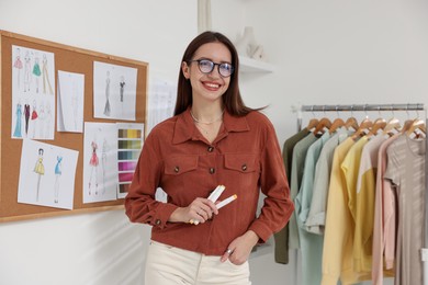 Photo of Fashion designer near corkboard with sketches of clothes in workshop