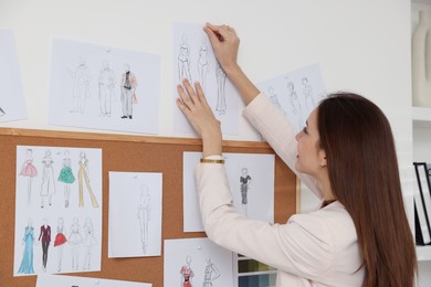 Photo of Fashion designer pinning sketch of clothes to wall in workshop