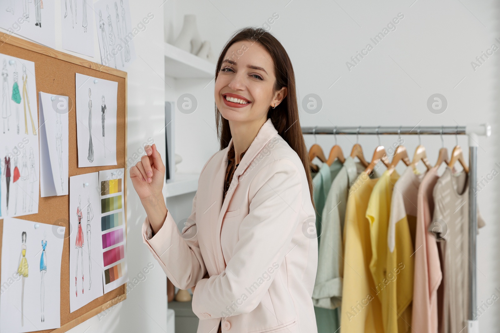 Photo of Fashion designer near corkboard with sketches of clothes in workshop