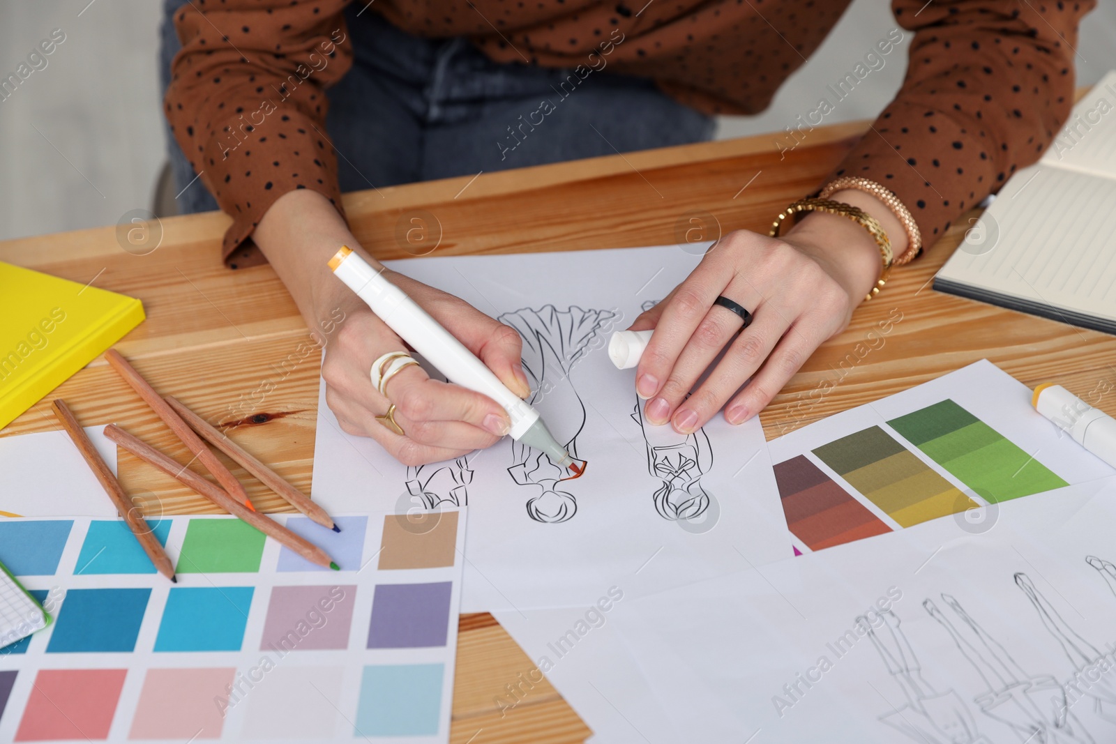 Photo of Fashion designer drawing sketch of clothes at wooden table in workshop, closeup