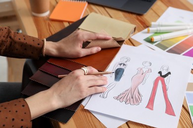 Photo of Fashion designer choosing fabric among colorful samples at wooden table in workshop, closeup