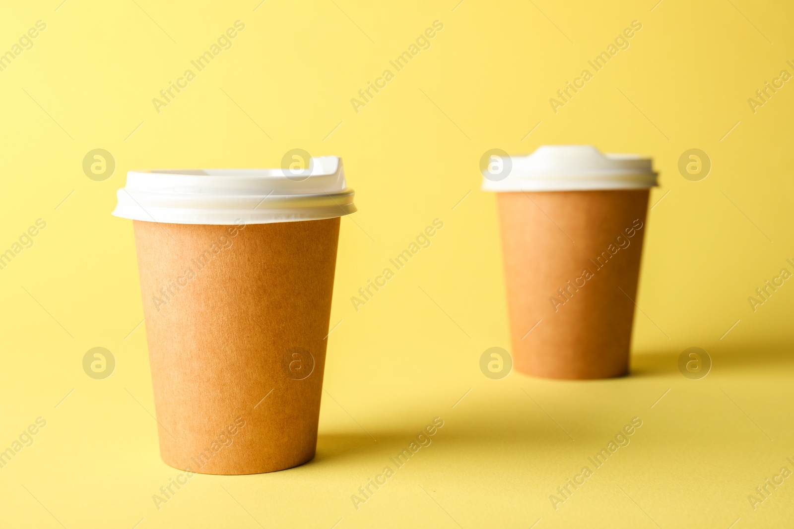 Paper cups on yellow background, selective focus. Mockup for design Photo of Paper cups on yellow background, selective focus. Mockup for design