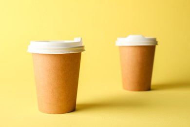 Photo of Paper cups on yellow background, selective focus. Mockup for design