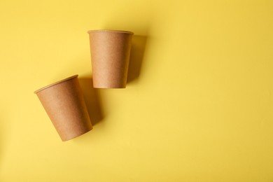 Photo of Paper cups on yellow background, flat lay. Mockup for design