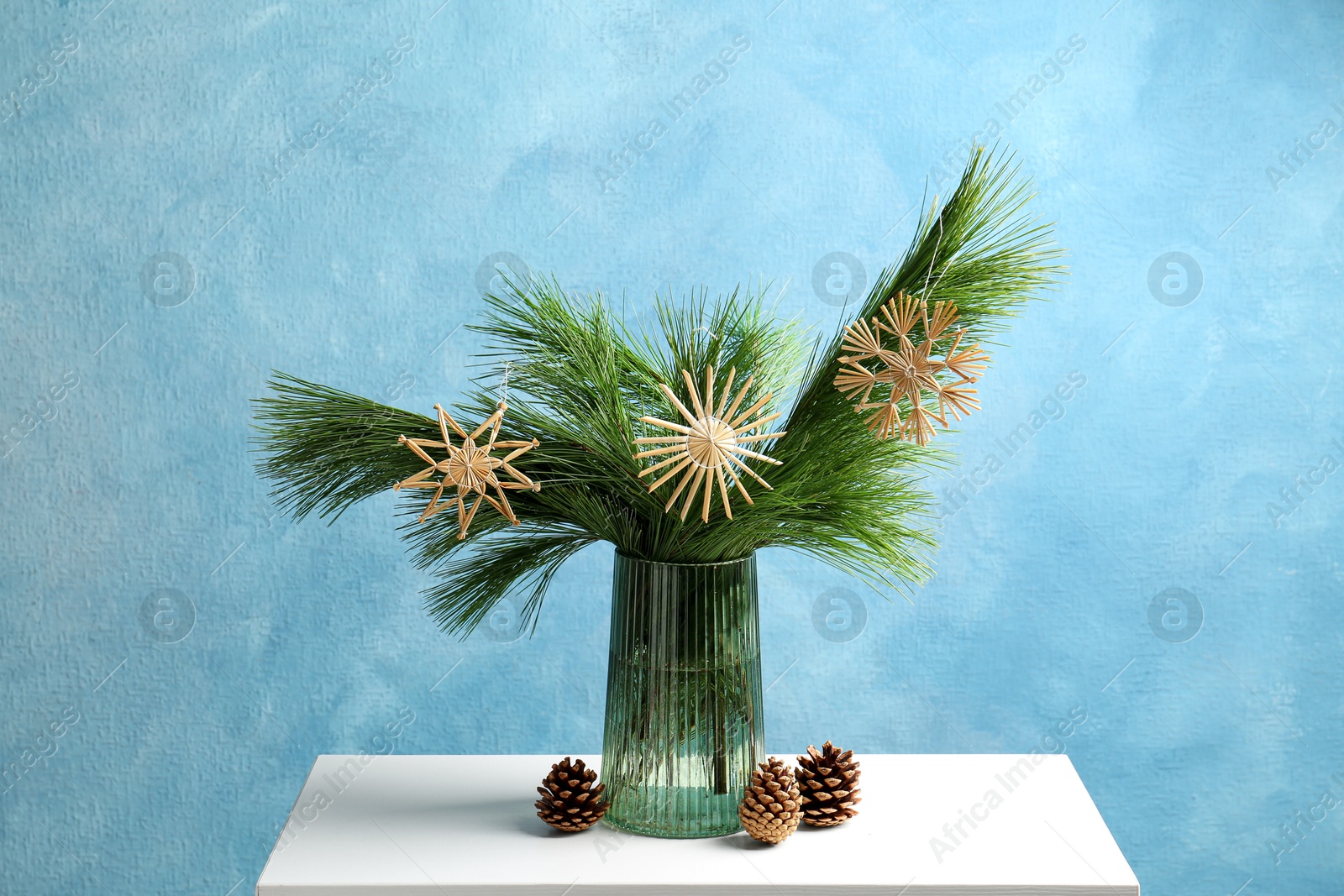 Photo of Beautiful decorated pine tree branches and cones on table near blue wall. Christmas season