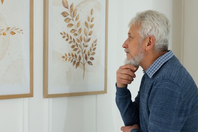 Photo of Senior man examining beautiful paintings in art gallery