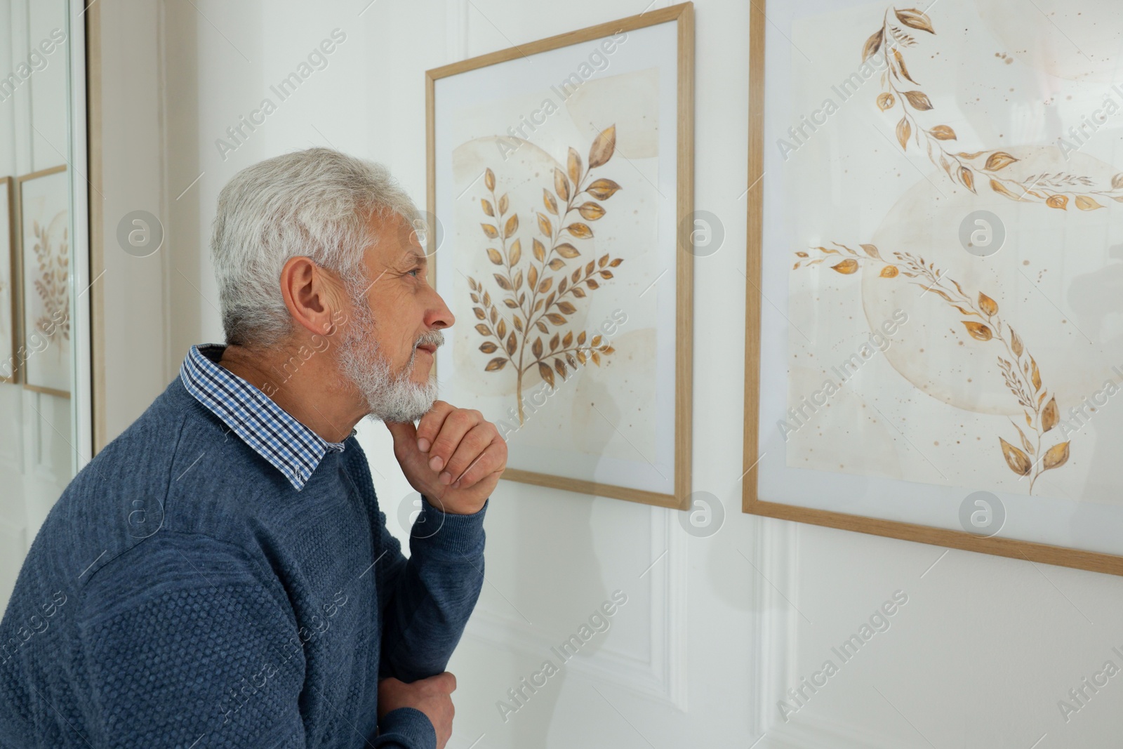 Photo of Senior man examining beautiful paintings in art gallery