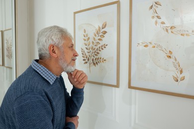 Photo of Senior man examining beautiful paintings in art gallery