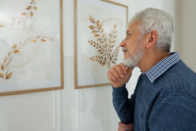 Photo of Senior man examining beautiful paintings in art gallery