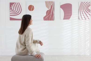 Photo of Woman sitting on pouf and looking at paintings in art gallery