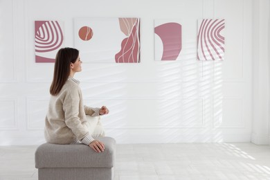 Photo of Woman sitting on pouf and looking at paintings in art gallery