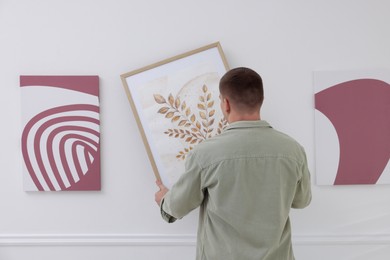 Photo of Man hanging painting on wall in art gallery, back view