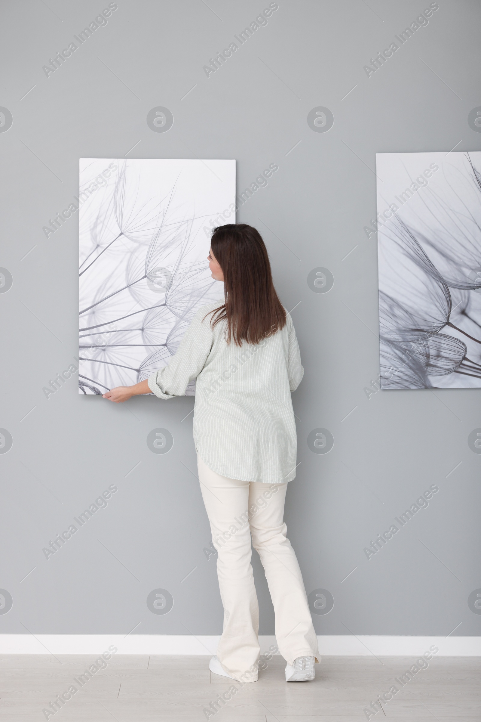 Photo of Woman hanging painting on wall in art gallery, back view