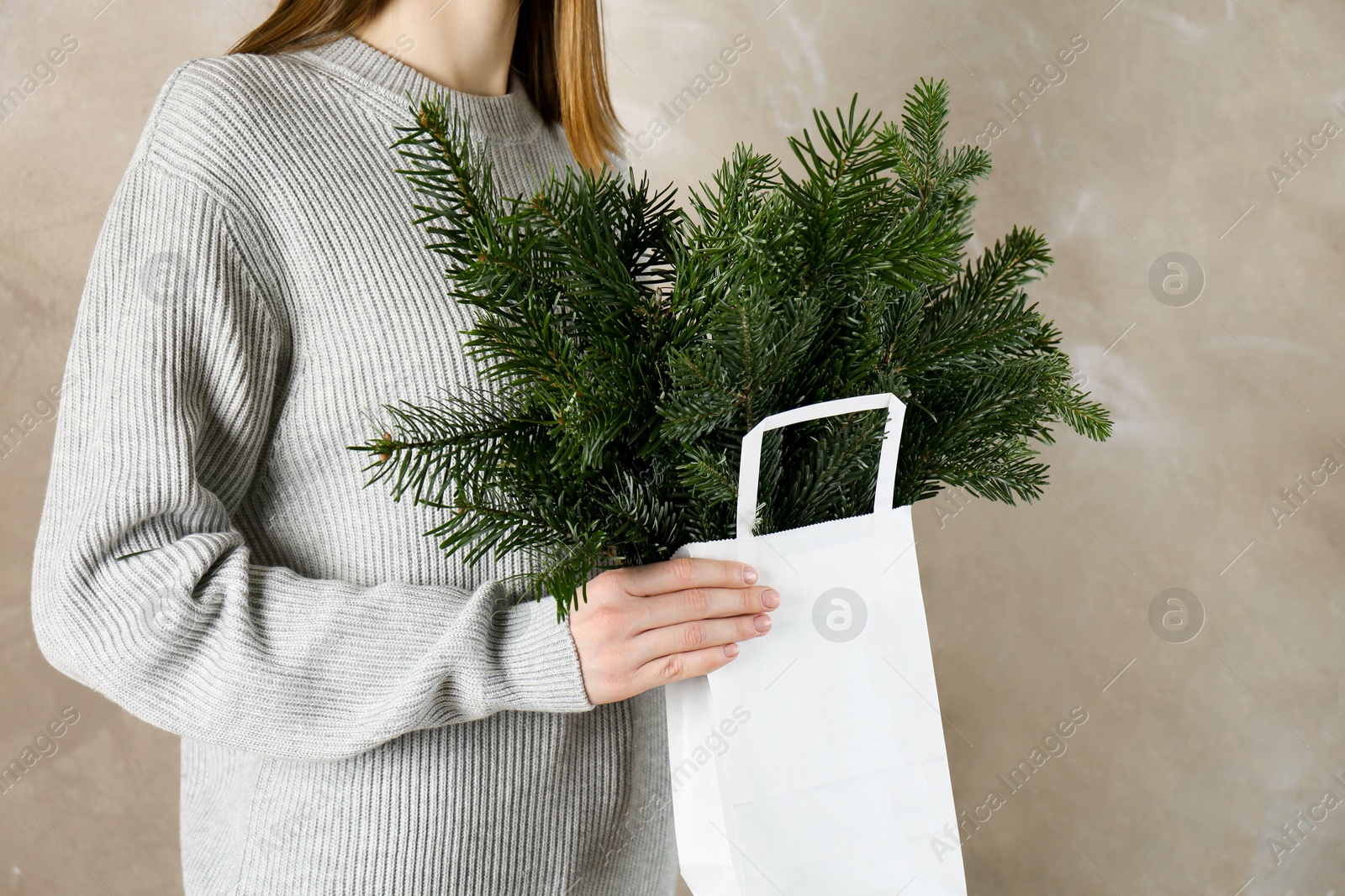 Photo of Woman holding green fir branches in paper bag near gray wall, closeup. Christmas decor