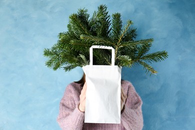 Photo of Woman holding green fir branches in paper bag near blue wall. Christmas decor