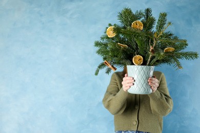 Photo of Woman holding beautiful Christmas composition of fir tree branches decorated with dried orange slices and cinnamon sticks near blue wall, space for text