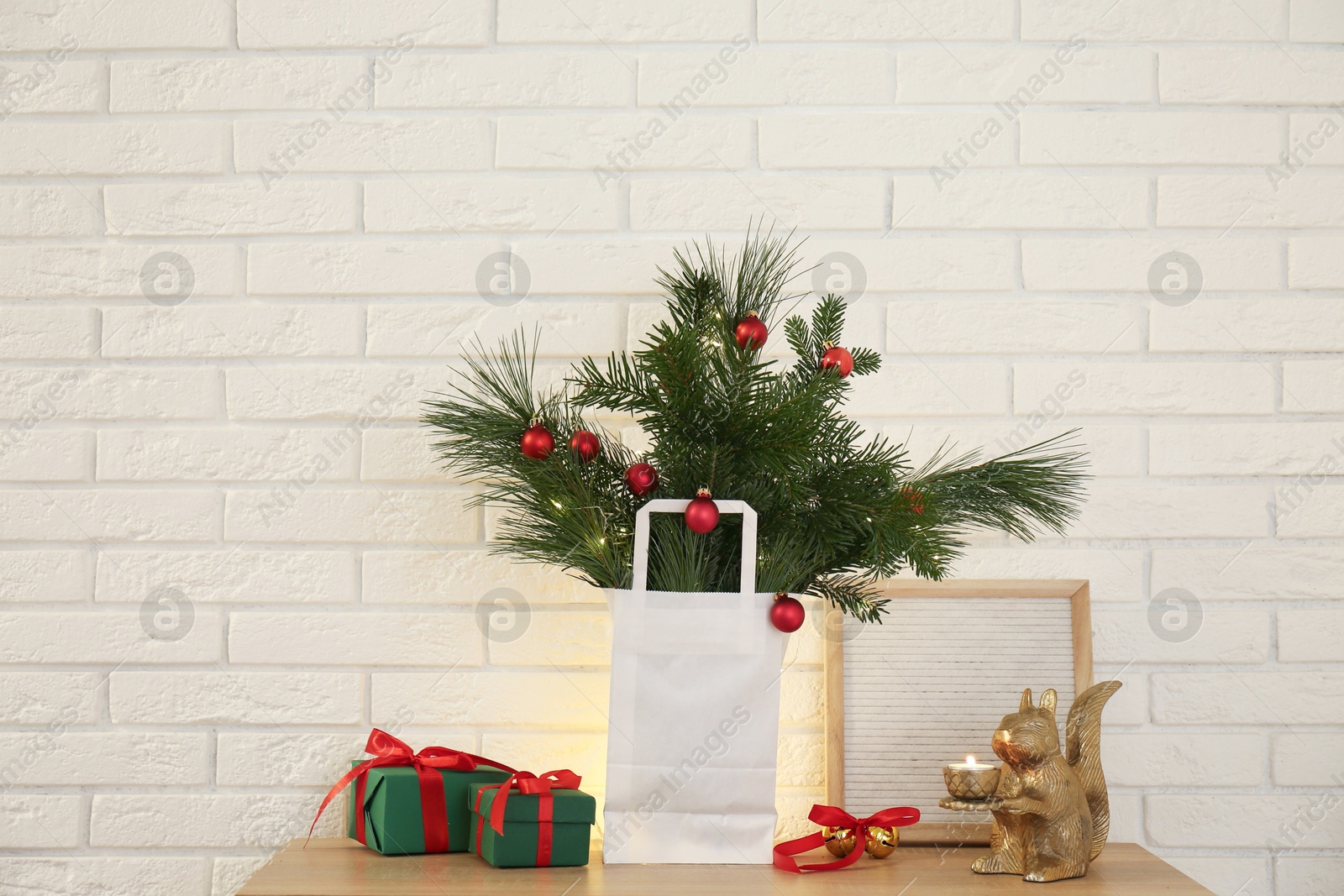 Photo of Beautiful Christmas composition of decorated fir and pine tree branches on wooden table near white brick wall