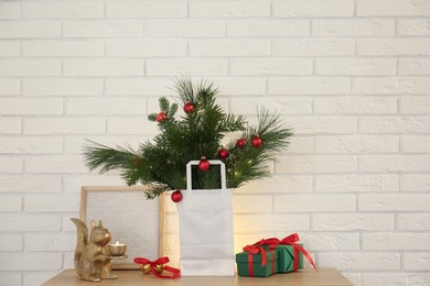 Photo of Beautiful Christmas composition of decorated fir and pine tree branches on wooden table near white brick wall