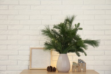 Photo of Beautiful Christmas composition of decorated fir and pine tree branches on wooden table near white brick wall