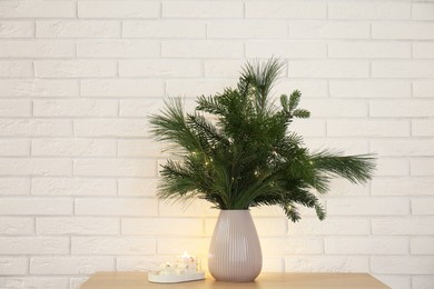 Photo of Beautiful Christmas composition of decorated fir and pine tree branches on wooden table near white brick wall