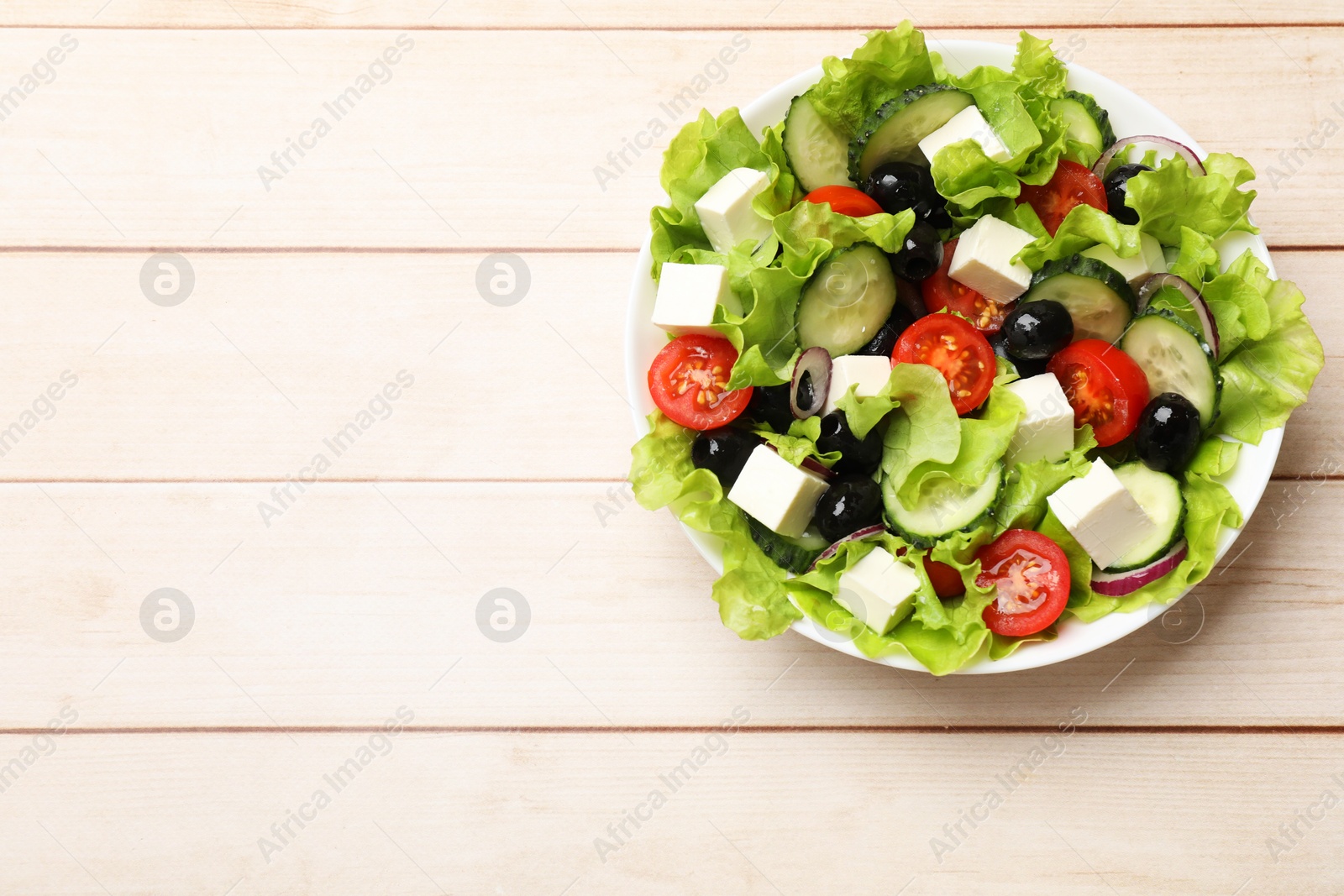 Photo of Delicious fresh Greek salad on light wooden table, top view. Space for text