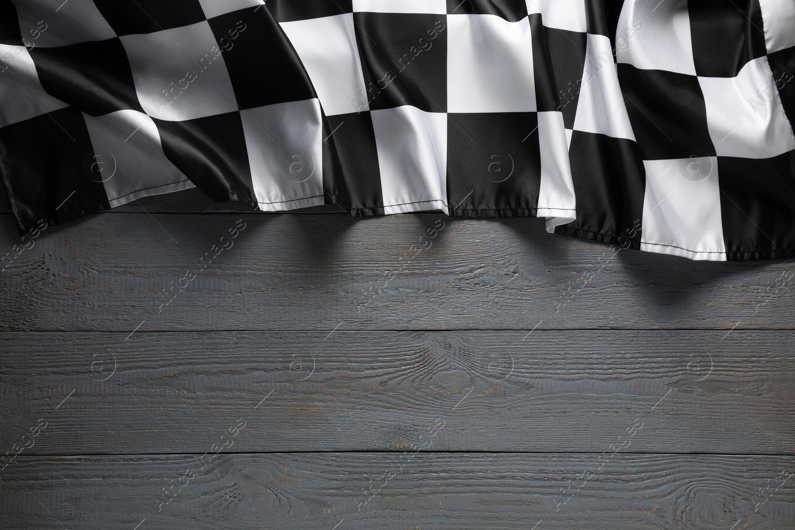 Photo of Checkered flag on grey wooden table, top view. Space for text