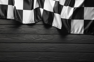 Photo of Checkered flag on black wooden table, top view. Space for text