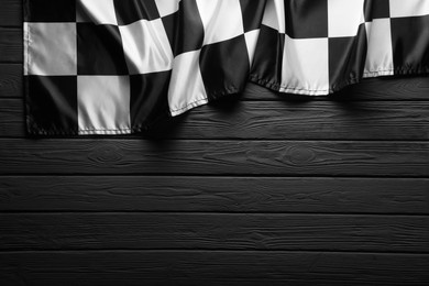 Photo of Checkered flag on black wooden table, top view. Space for text