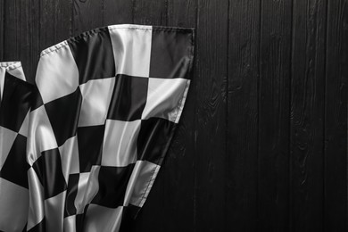 Photo of Checkered flag on black wooden table, top view. Space for text