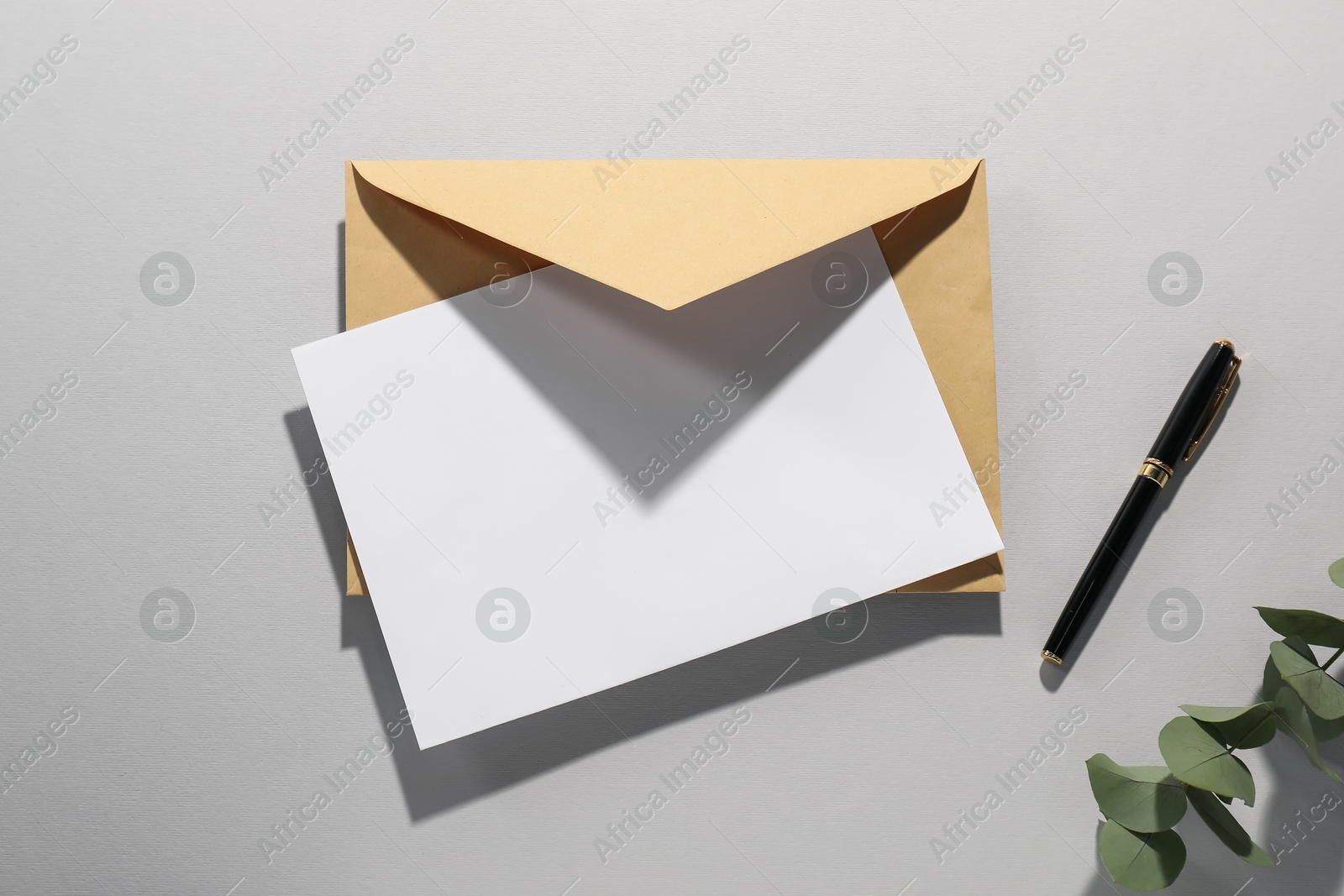 Photo of Kraft paper envelope, letter, pen and eucalyptus branch on grey background, flat lay. Mockup for design