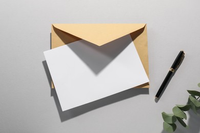 Kraft paper envelope, letter, pen and eucalyptus branch on grey background, flat lay. Mockup for design