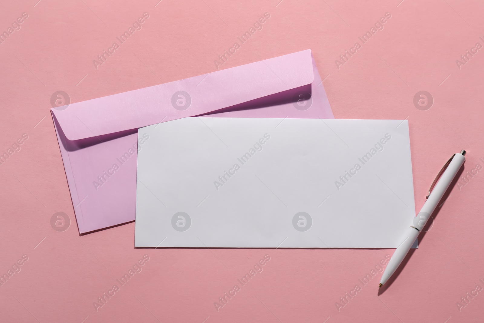 Photo of Paper envelopes and pen on pink background, top view. Mockup for design