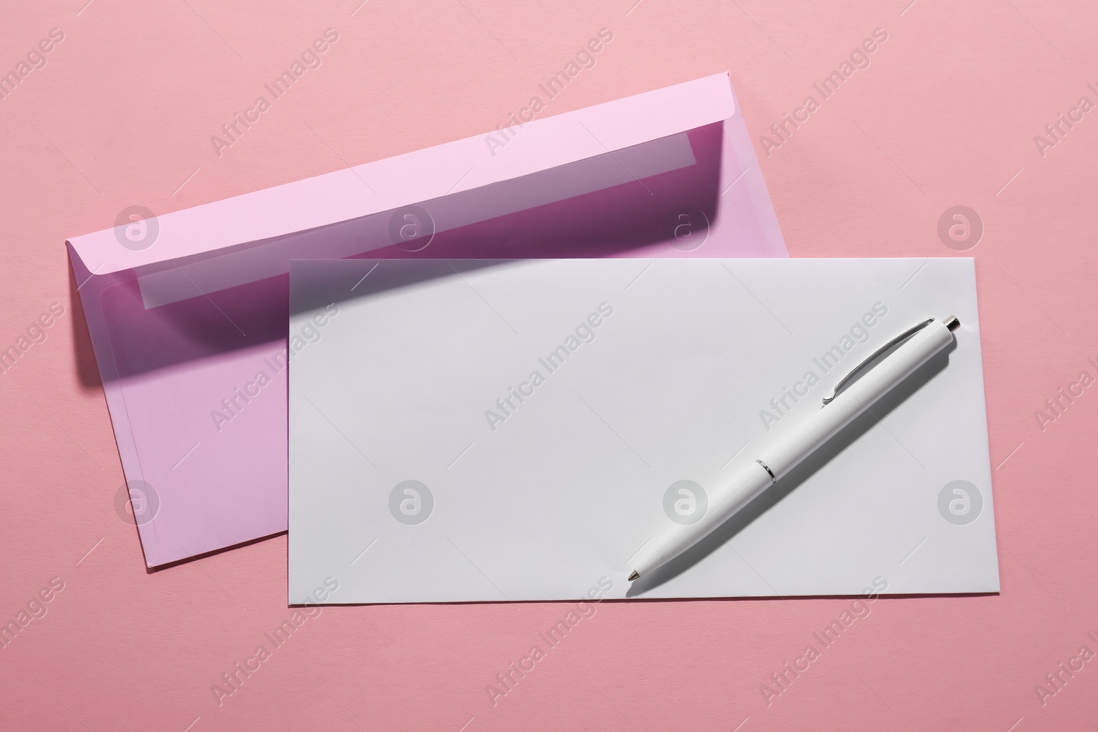 Photo of Paper envelopes and pen on pink background, top view. Mockup for design