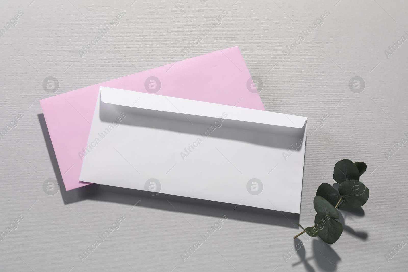 Photo of Paper envelopes and eucalyptus branch on grey background, top view. Mockup for design