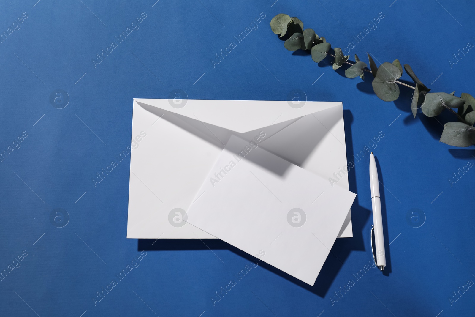 Photo of Paper envelope with letter, eucalyptus branch and pen on blue background, flat lay. Mockup for design