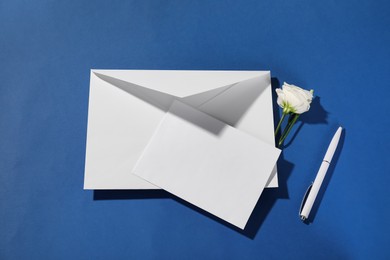 Photo of Paper envelope with letter, flower and pen on blue background, flat lay. Mockup for design