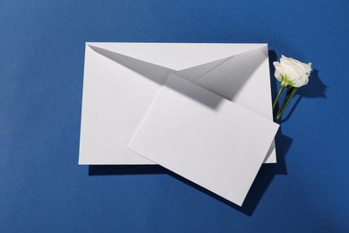 Paper envelope with letter and flower on blue background, top view. Mockup for design