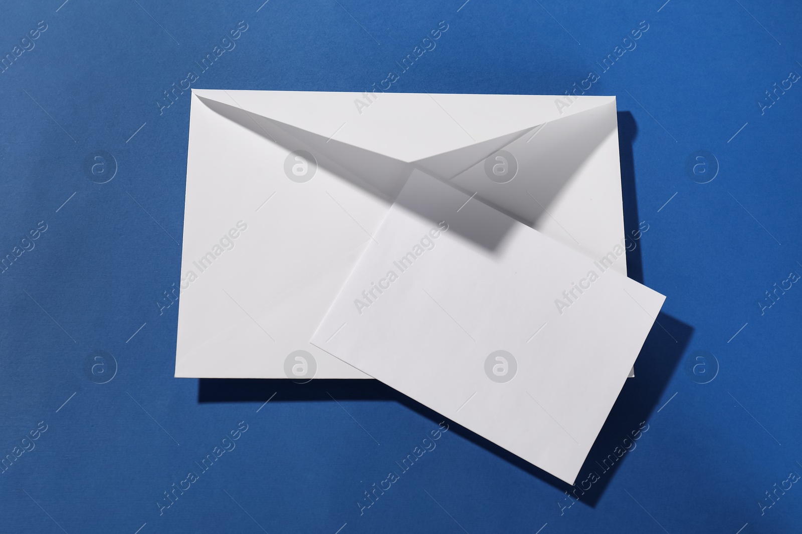 Photo of Paper envelope with letter on blue background, top view. Mockup for design