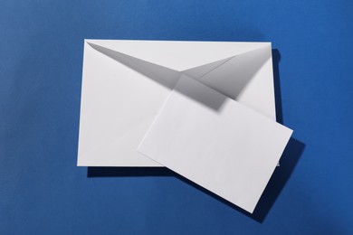 Paper envelope with letter on blue background, top view. Mockup for design