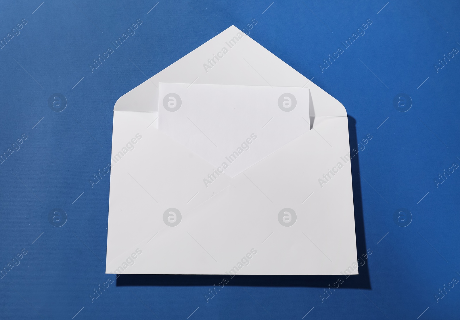 Photo of Paper envelope with letter on blue background, top view. Mockup for design