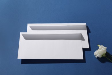 Photo of Paper envelopes and flower on blue background, above view. Mockup for design