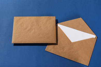 Photo of Kraft paper envelopes with letter on blue background, top view. Mockup for design