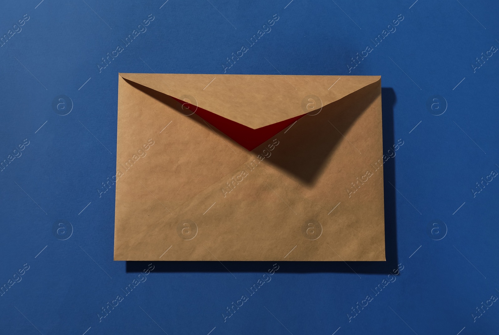 Photo of Kraft paper envelope on blue background, top view. Mockup for design